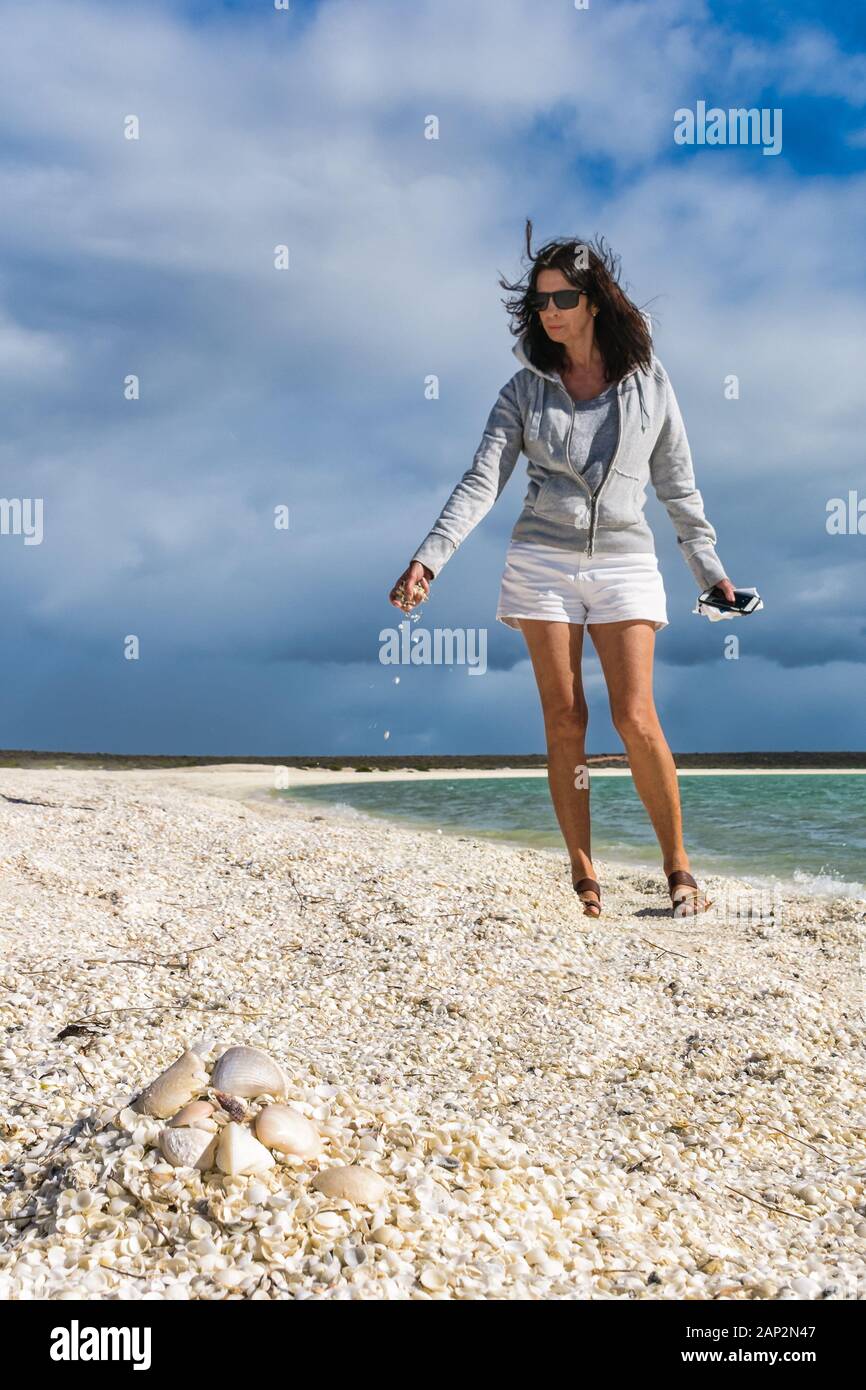 Image basse perspective de touriste féminin avec une poignée de coquilles de coqles tombant sur la plage de Shelkl à Shark Bay en Australie occidentale. Banque D'Images