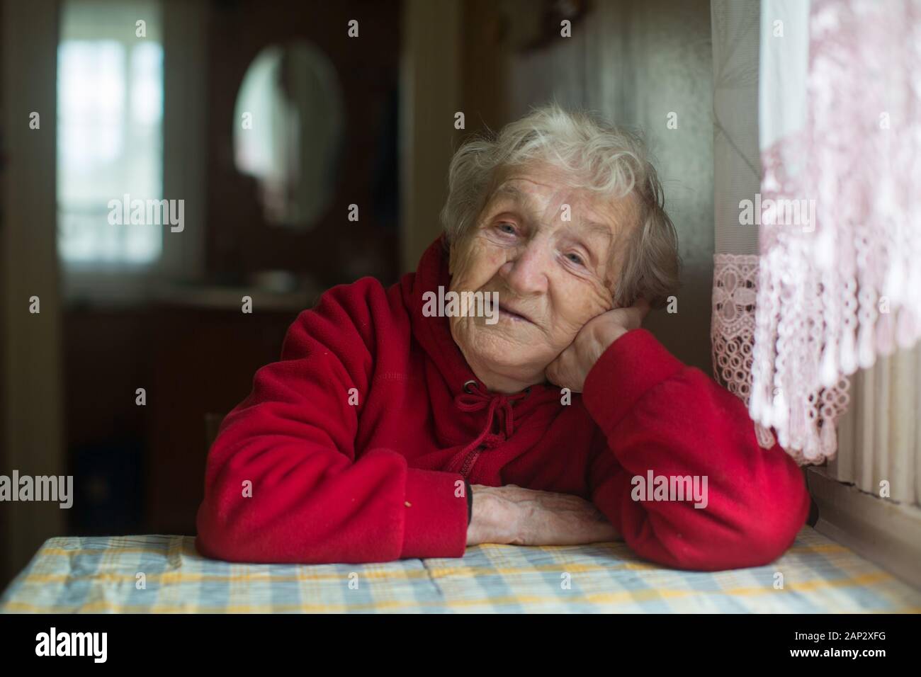 Portrait d'une vieille femme assise à une table dans la chambre. Banque D'Images
