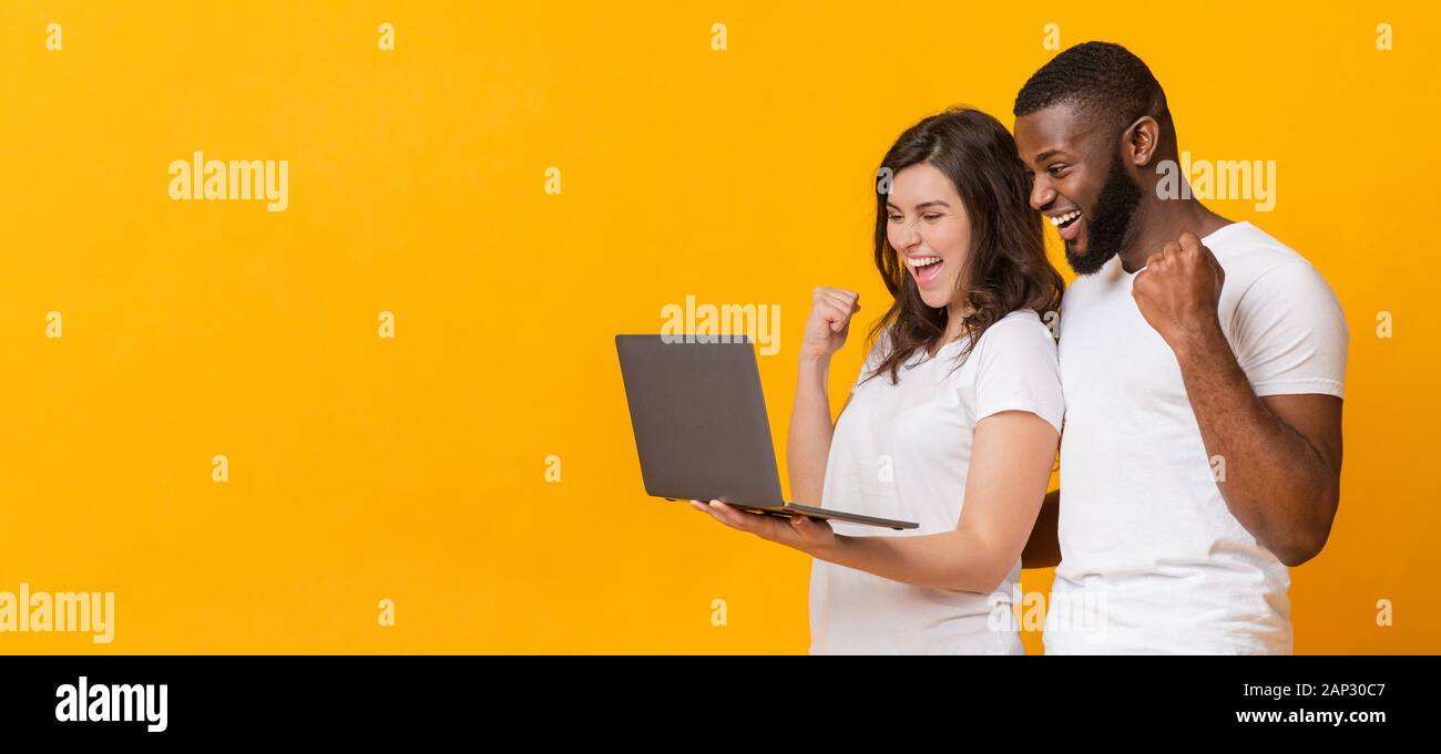 Couple multiracial joyeuse allégresse succès avec ordinateur portable, s'exclamant avec excitation Banque D'Images
