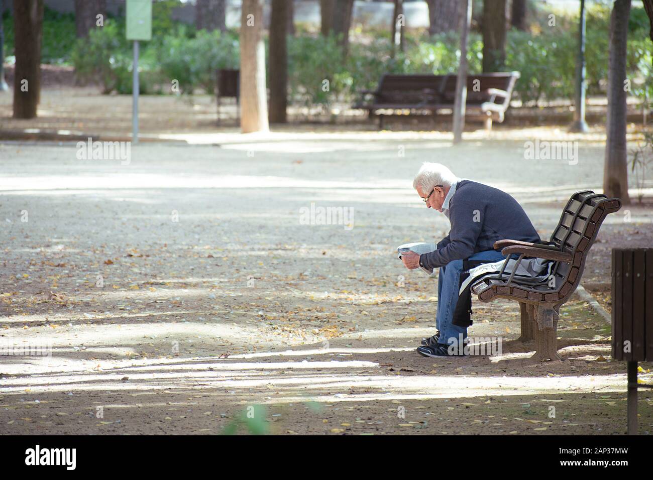 Albacete, Espagne, le 18 janvier 2020 : Senior homme assis sur un banc en bois, de lire le journal dans le parc Abelardo Sanchez Banque D'Images