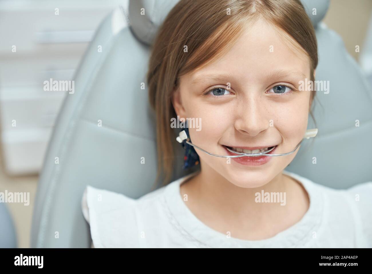 Jolie petite fille avec de beaux yeux bleus assis dans une chaise dentaire  avec des bretelles orthodontiques pour améliorer la morsure. Une jeune  jolie dame qui s'occupe des dents dans une clinique