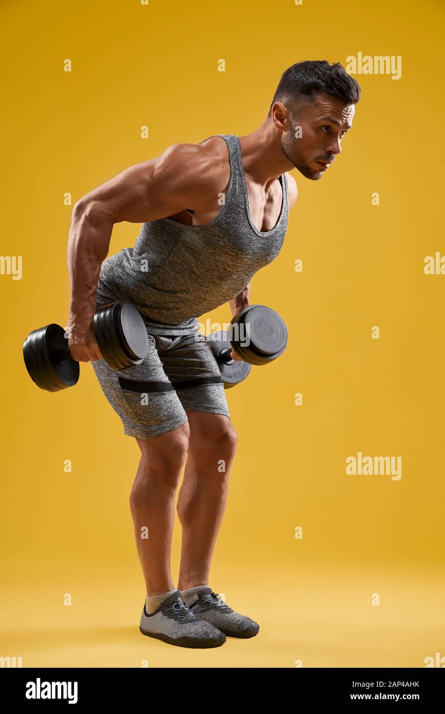 Vue latérale de beau bodybuilder pompant les muscles. Un gars musclé et brutal qui fait de l'exercice de musculation. Isolé sur fond de studio jaune. Concept de sport et de culturisme. Banque D'Images