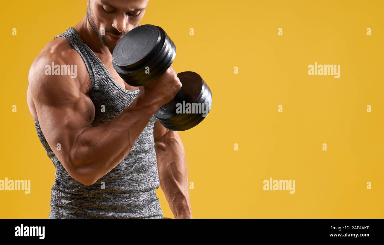 Gros plan sur le jeune homme athlétique qui pèse lourd. Un homme musclé qui pompe des biceps. Isolé sur fond de studio jaune avec espace de copie. Concept de sport et de culturisme. Banque D'Images