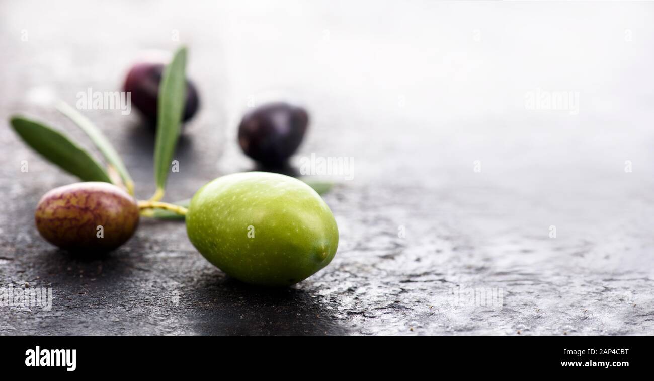 Gros plan de fruits d'olive frais sur fond sombre texturé avec copyspace. Olives biologiques noires et vertes à feuilles. Cuisine espagnole. Banque D'Images