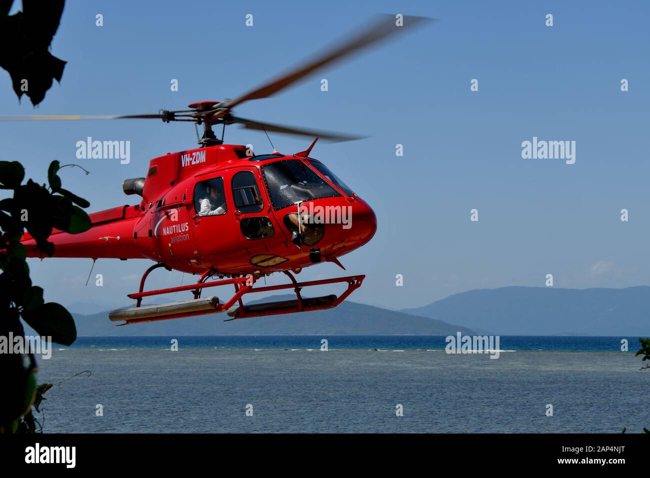 Atterrissage en hélicoptère rouge après un vol panoramique au-dessus de la Grande barrière de corail, Queensland, Australie avec eau et montagnes dans la batchground Banque D'Images