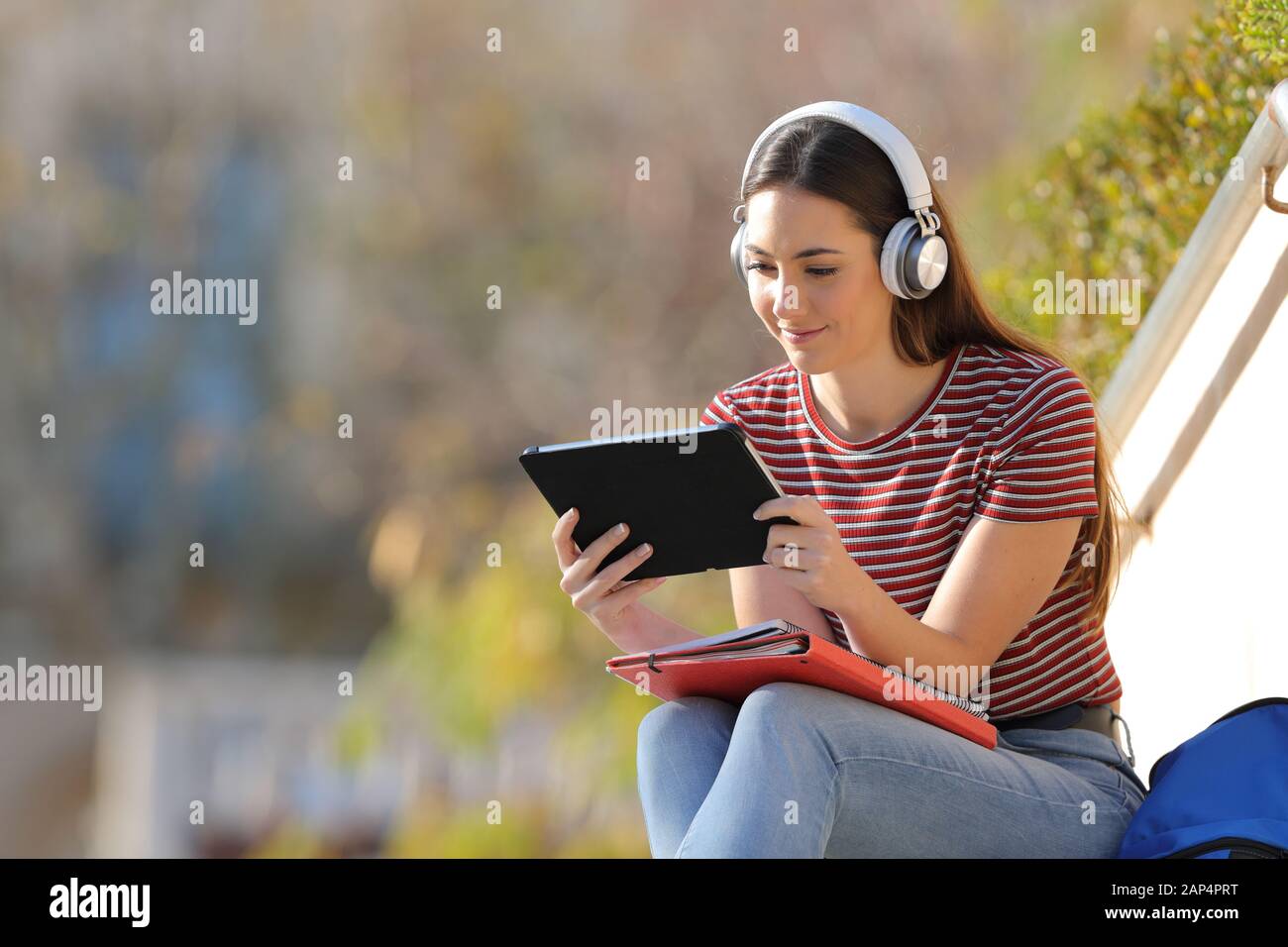 E-learning étudiant sérieux avec tablette et casque assis sur un campus une journée ensoleillée Banque D'Images