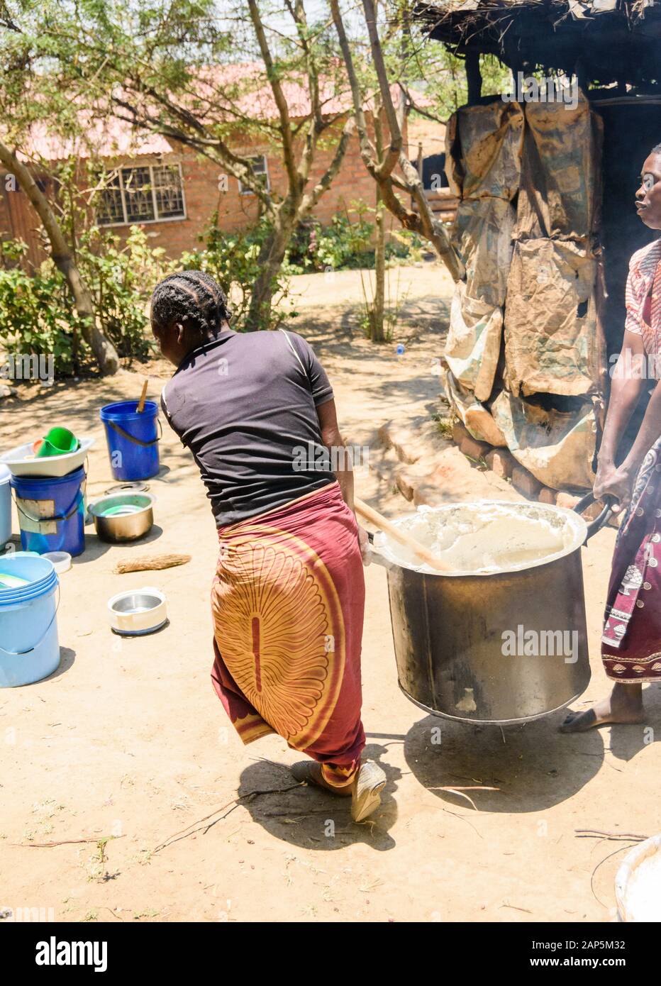 Un portrait de deux femmes malawiennes portent un pot en métal très lourd de porridge de maïs vapeur dans un cadre de village Banque D'Images