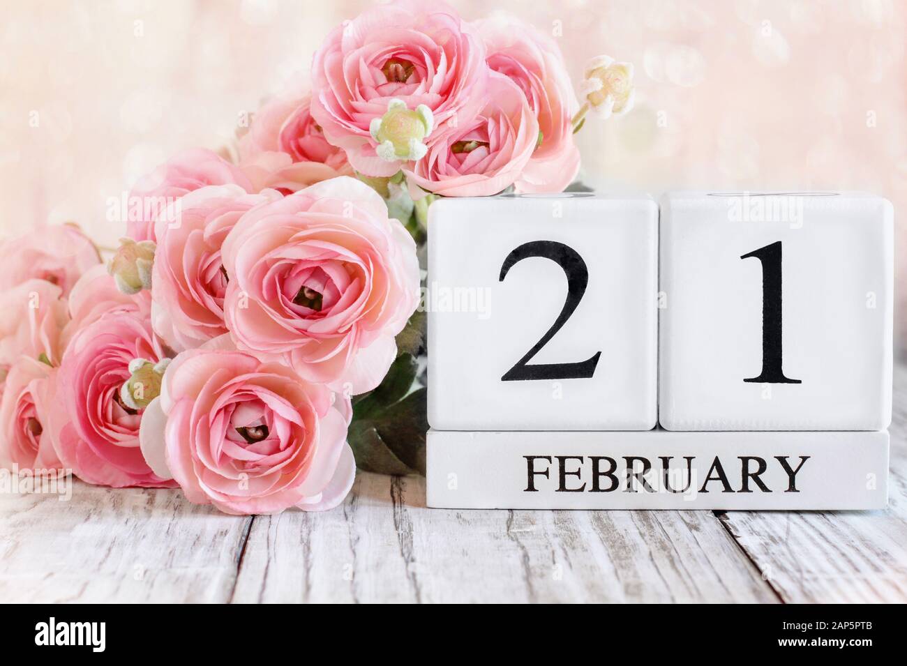 Blocs calendrier en bois blanc avec la date du 21 février et fleurs roses de ranunculus sur une table en bois. Mise au point sélective avec arrière-plan flou. Banque D'Images