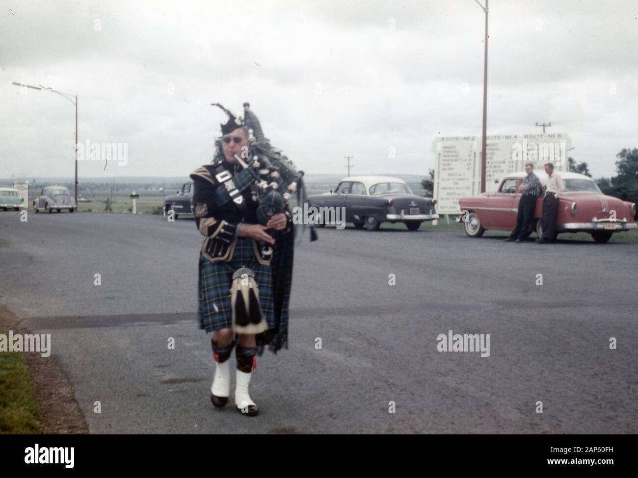 Un bagpiper dans une robe écossaise traditionnelle complète promenades à côté d'une route, 1965. () Banque D'Images