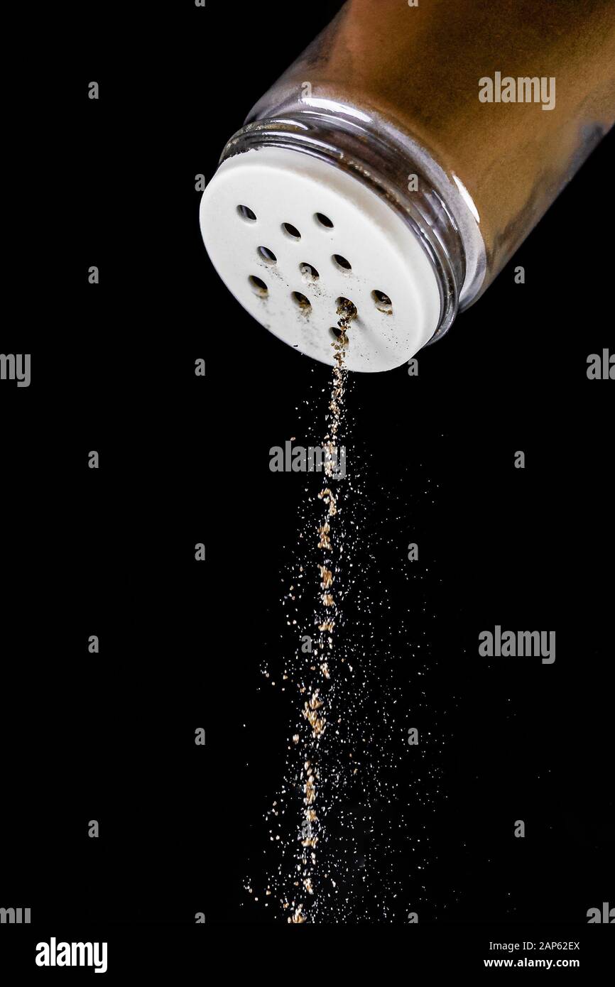 Le poivre noir est sorti de l'agitateur à poivre sur un fond noir isolé. Le processus d'assaisonnement s'arrête à temps. Agitateur à sel de verre avec St blanc Banque D'Images