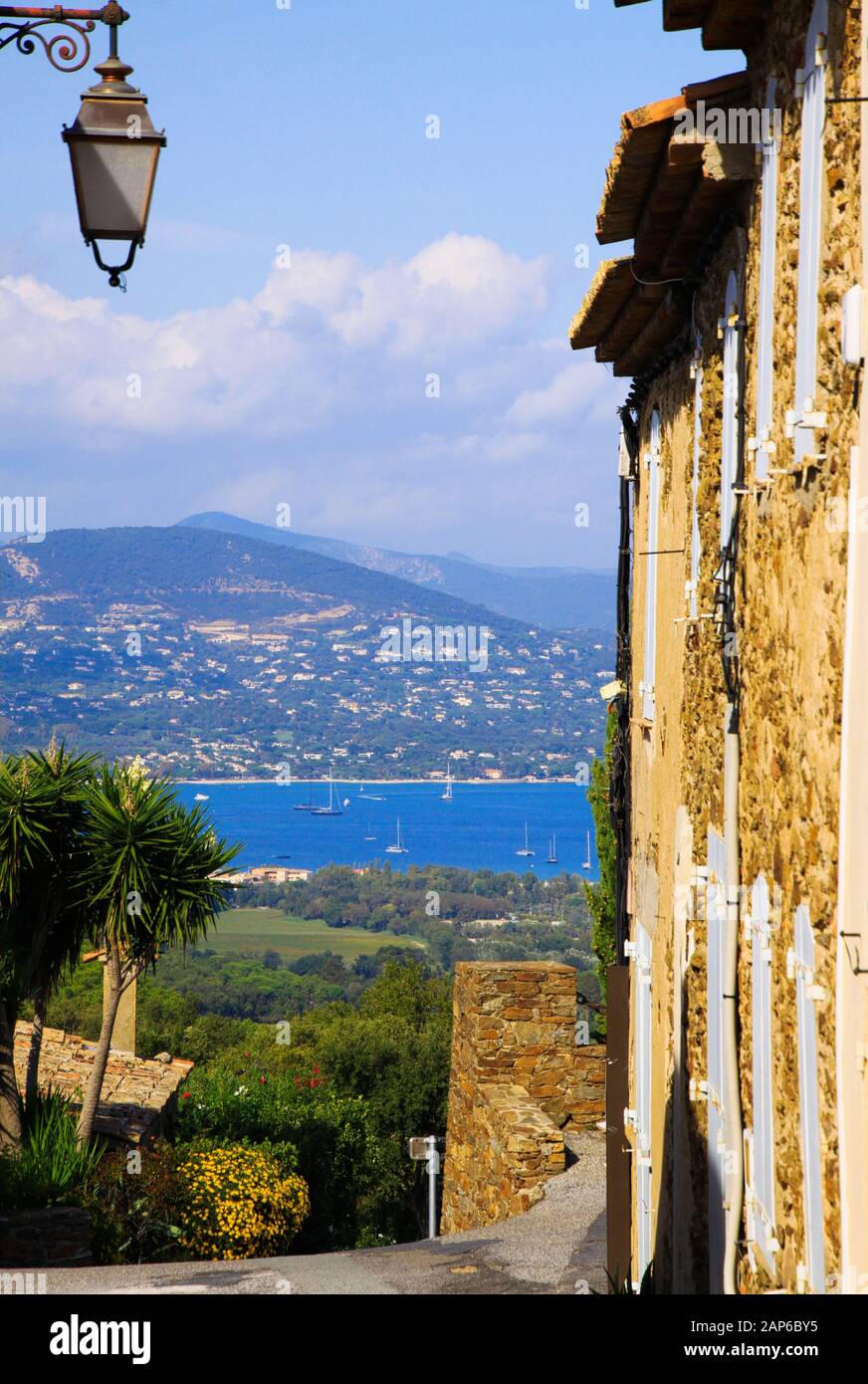 Vue au-delà de l'ancien mur de maison et lampe de rue du village de haut de colline méditerranéen Gassin sur la mer bleue du golfe de Saint-Tropez. Montagne floue avec cors Banque D'Images