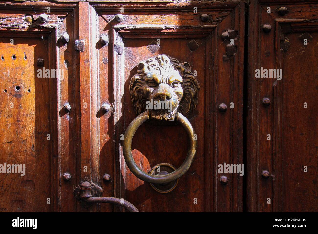 Gros plan sur le knocker de porte en fer en métal antique en forme de tête de lion avec anneau sur l'ancienne entrée en bois avec encoches dans lumière naturelle vive du soleil - Provence, Banque D'Images