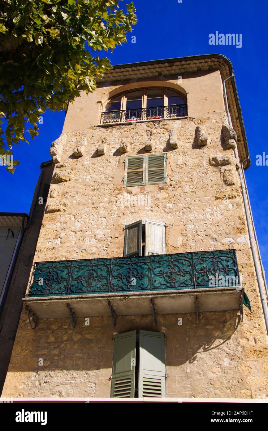 Vue à bas angle sur la façade en pierre de la maison française typique et balcon avec des travaux de treillis ornementé contre le ciel bleu et l'arbre vert - Castellane, Fran Banque D'Images