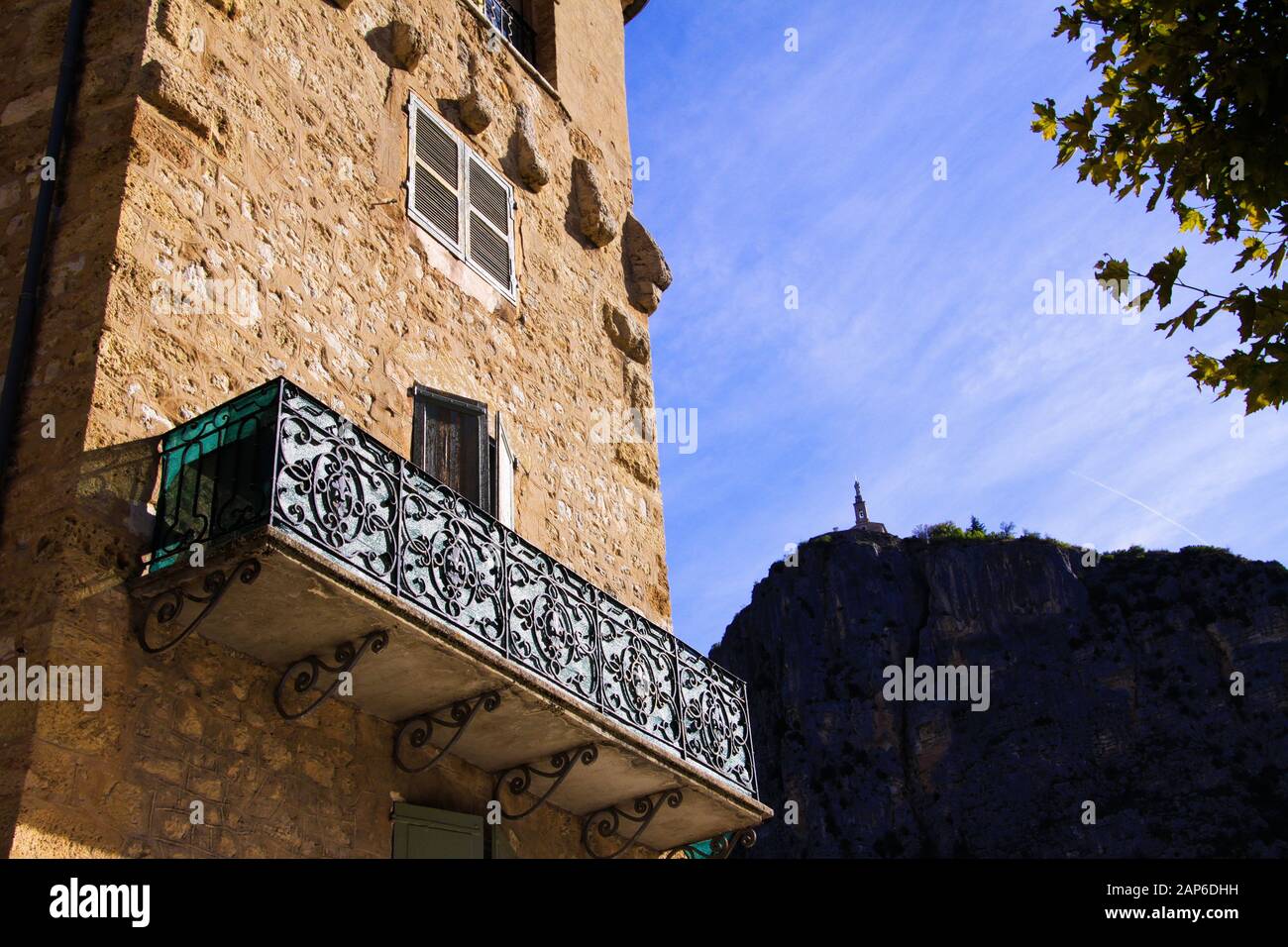 Vue à bas angle sur la façade en pierre de la maison française typique et balcon avec travaux de treillis anciens. Église sur fond de montagne - Castellane, F Banque D'Images