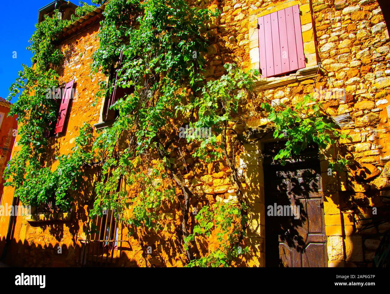 Vue sur la façade de la maison française en pierre naturelle méditerranéenne avec volets roses, porte en bois et plante de vigne grimpant mur - Roussillon en Proven Banque D'Images