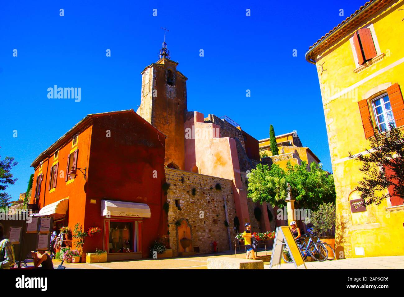 Roussillon En Provence, France - 2 Octobre. 2019: Vue au-delà de la maison jaune lumineuse méditerranéenne sur la tour de l'église d'ocre contre le ciel bleu Banque D'Images