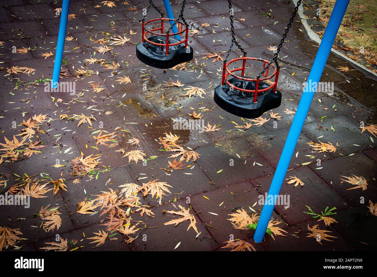 Les enfants vides se balancent sur une aire de jeux déserte avec des feuilles d'automne sur le sol après la pluie. Banque D'Images