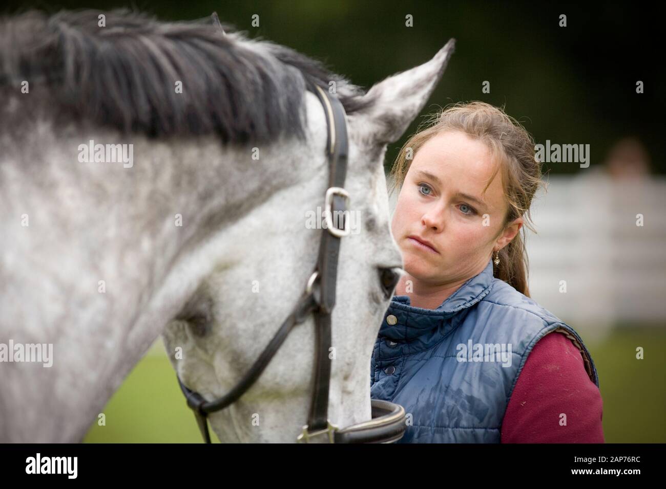 Jeune femme à la recherche de son cheval gris tout en se tenant dans un enclos. Banque D'Images