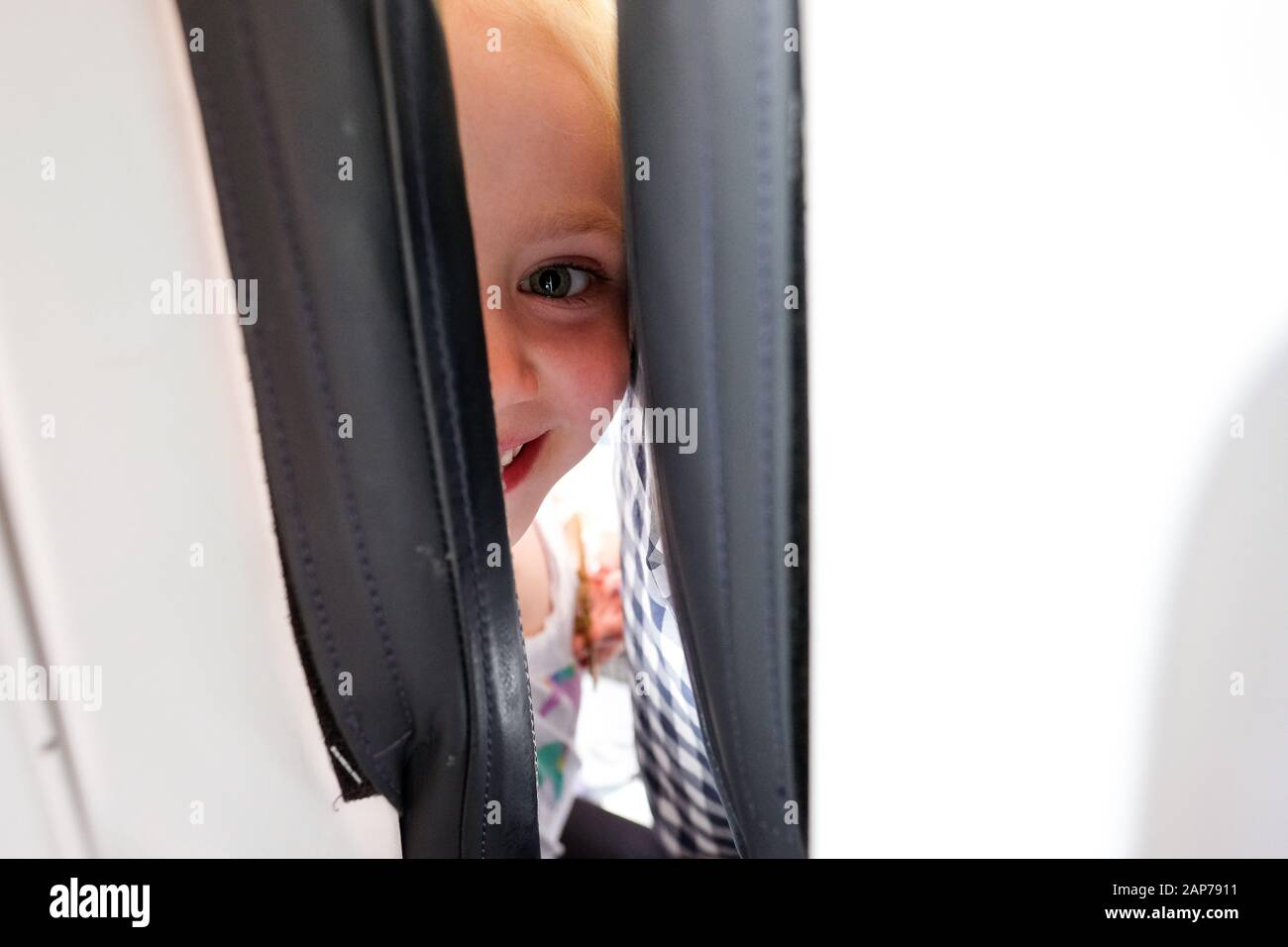petite fille souriant et regardant l'appareil photo entre les sièges sur l'avion Banque D'Images