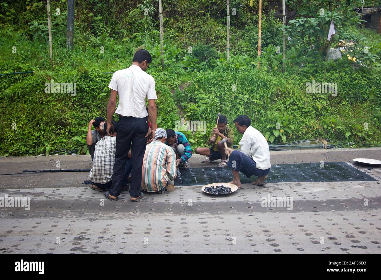 Un groupe d'hommes qui répare une route. Ils pirent des roches dans le goudron, l'asphalte, pour une meilleure traction. À Darjeeling, Bengale Occidental, Inde. Banque D'Images