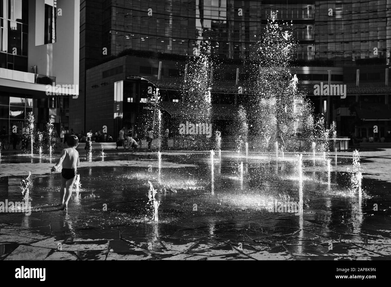 Bébé courant autour des jets d'eau de la fontaine sur la place Gae Aulenti - Milan, Italie Banque D'Images