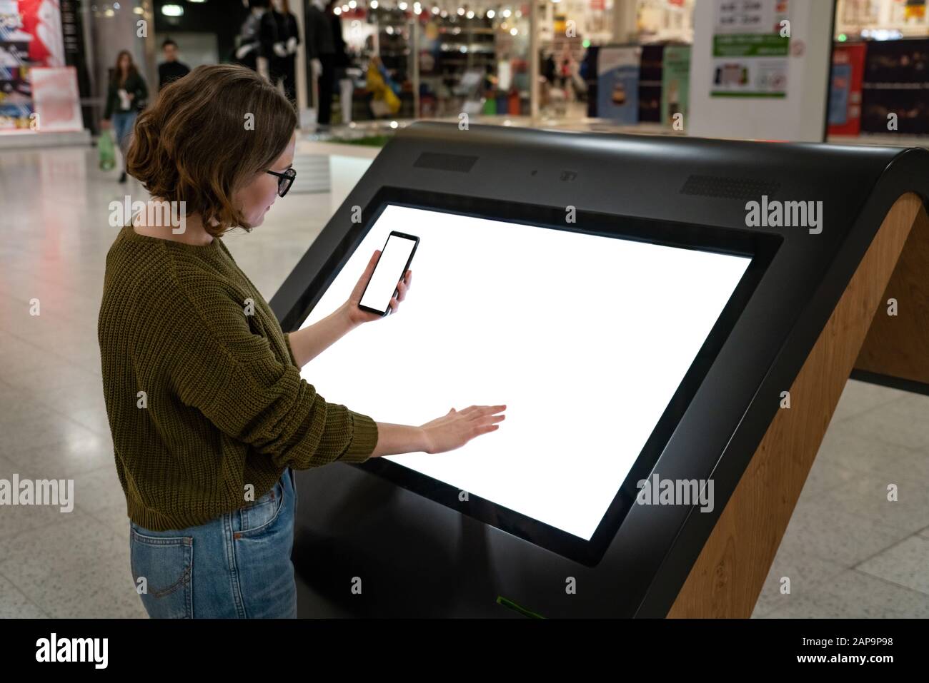 Une femme avec téléphone utilise un kiosque en libre-service dans le centre commercial Banque D'Images
