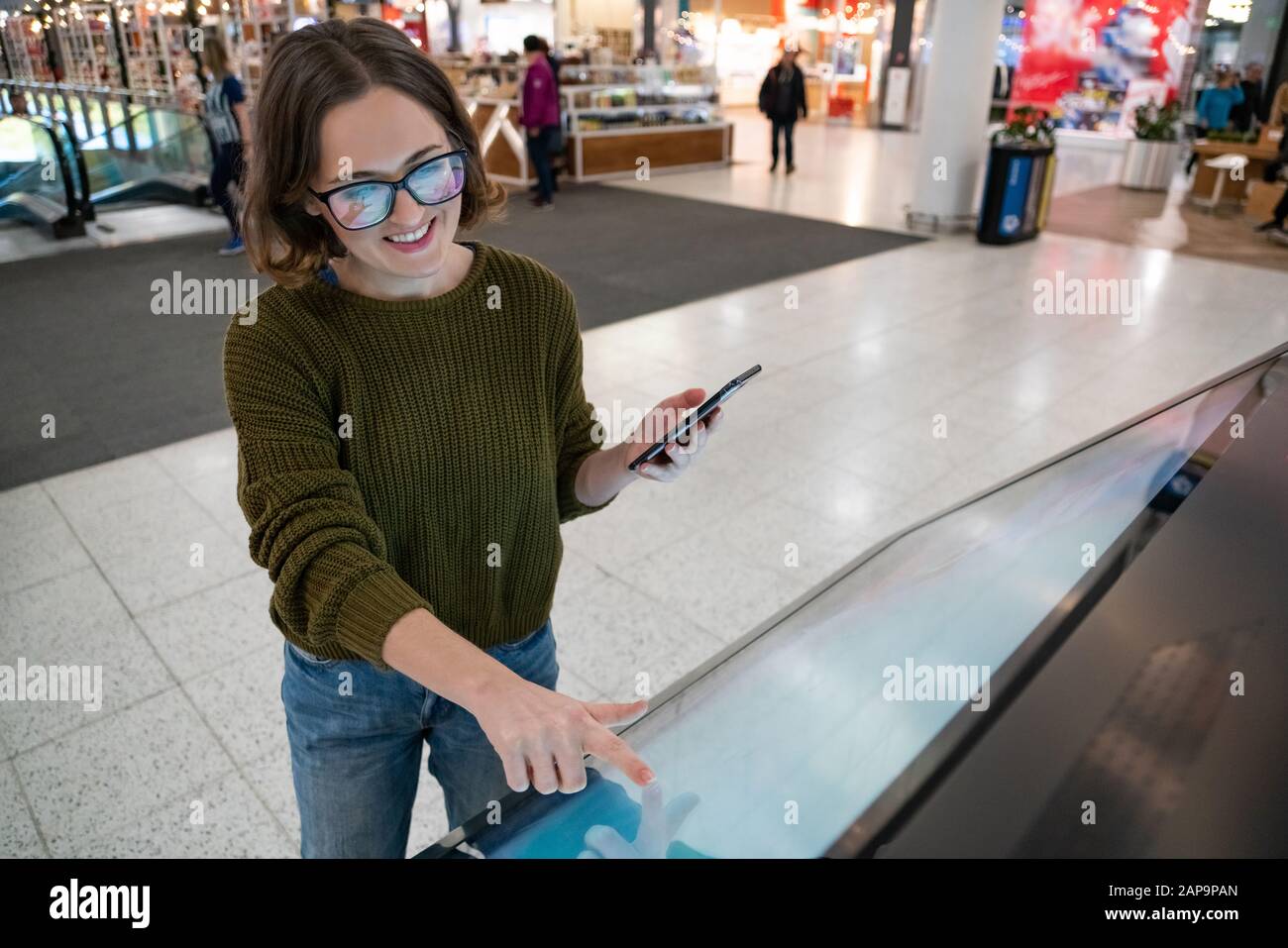 Une femme avec téléphone utilise un kiosque en libre-service dans le centre commercial Banque D'Images