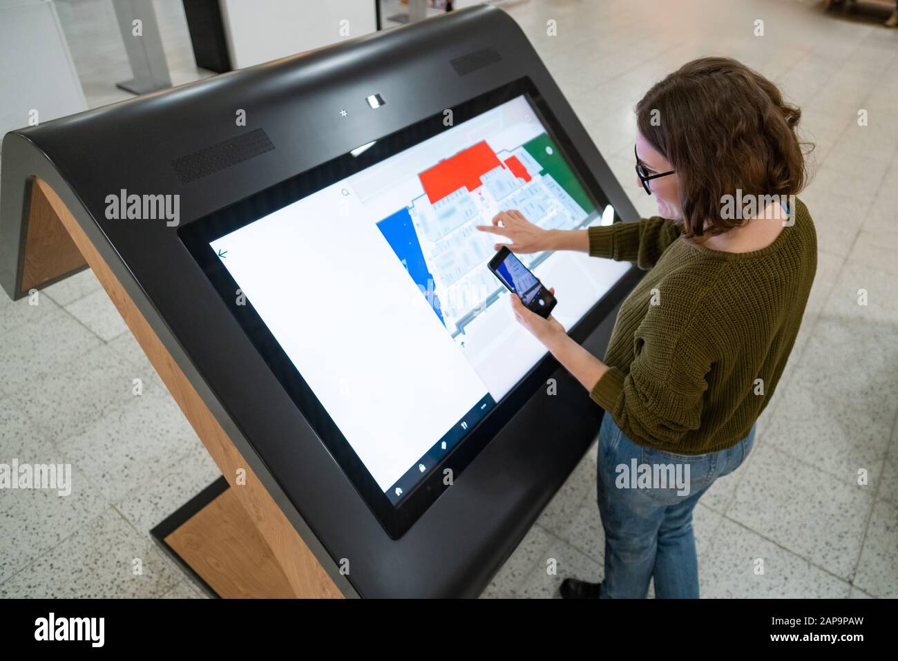 Une femme avec téléphone utilise un kiosque en libre-service dans le centre commercial Banque D'Images