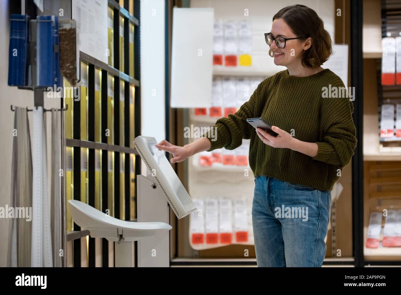 Une femme avec téléphone utilise un kiosque en libre-service dans le centre commercial Banque D'Images