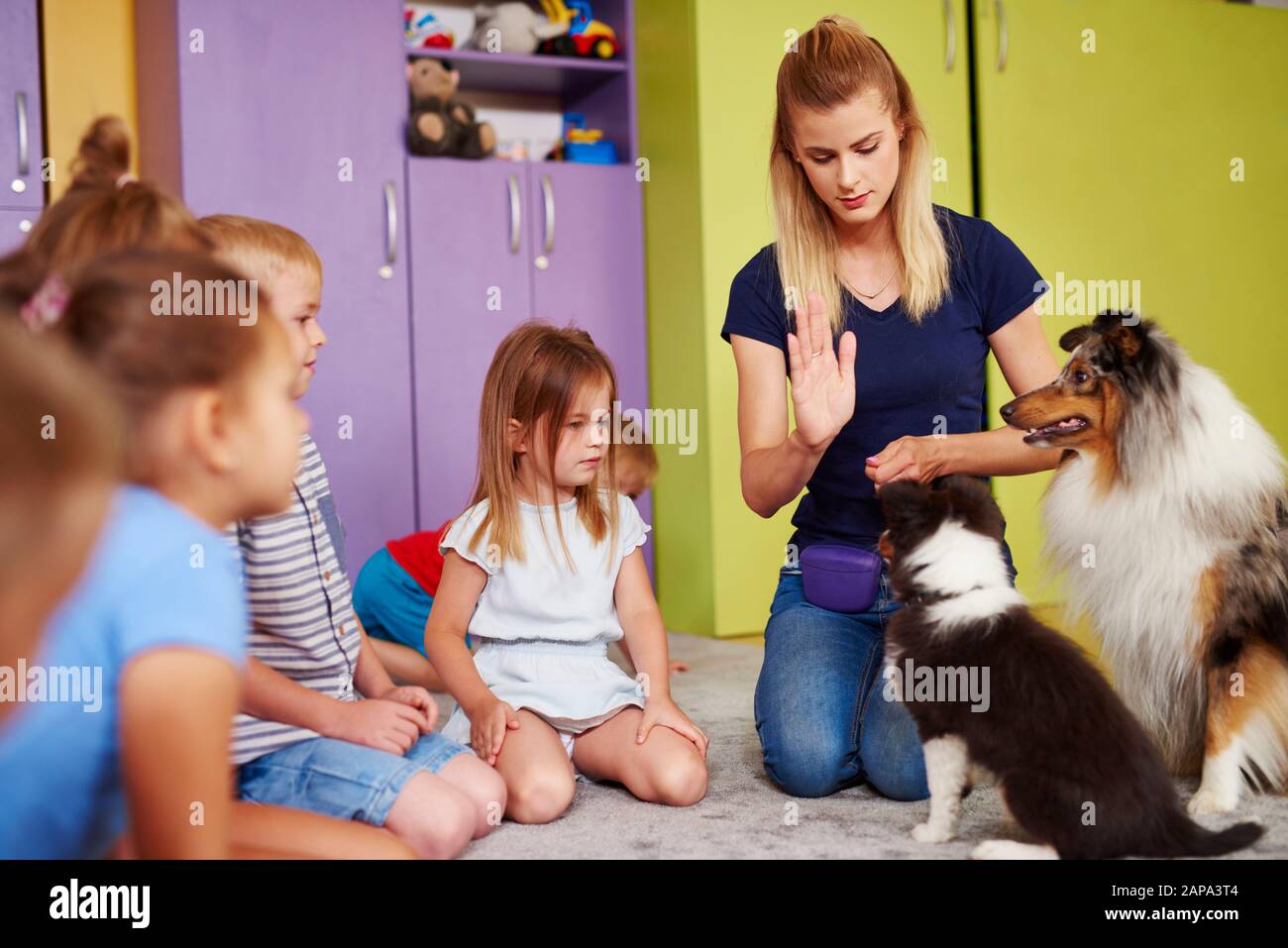Thérapeute féminin et son chien jouant avec des enfants dans la maternelle Banque D'Images