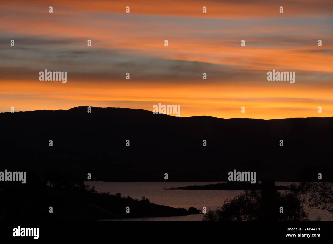 Des oranges lumineuses coucher de soleil au bord du lac Jindabyne dans les montagnes enneigées australie Banque D'Images