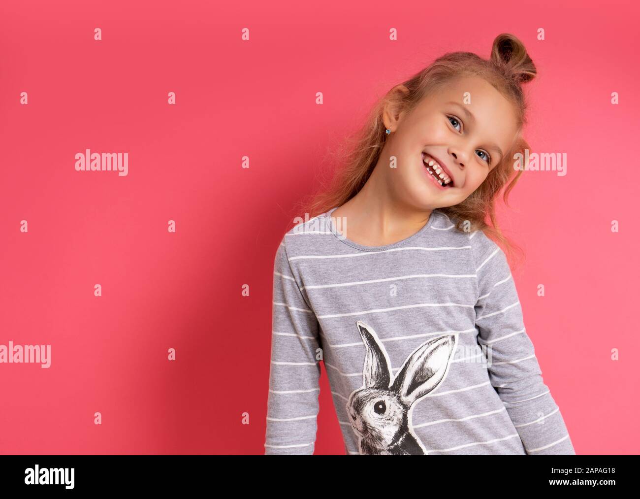 Drôle petite fille avec une drôle de coiffure se tenant sourire sur un fond rose Banque D'Images