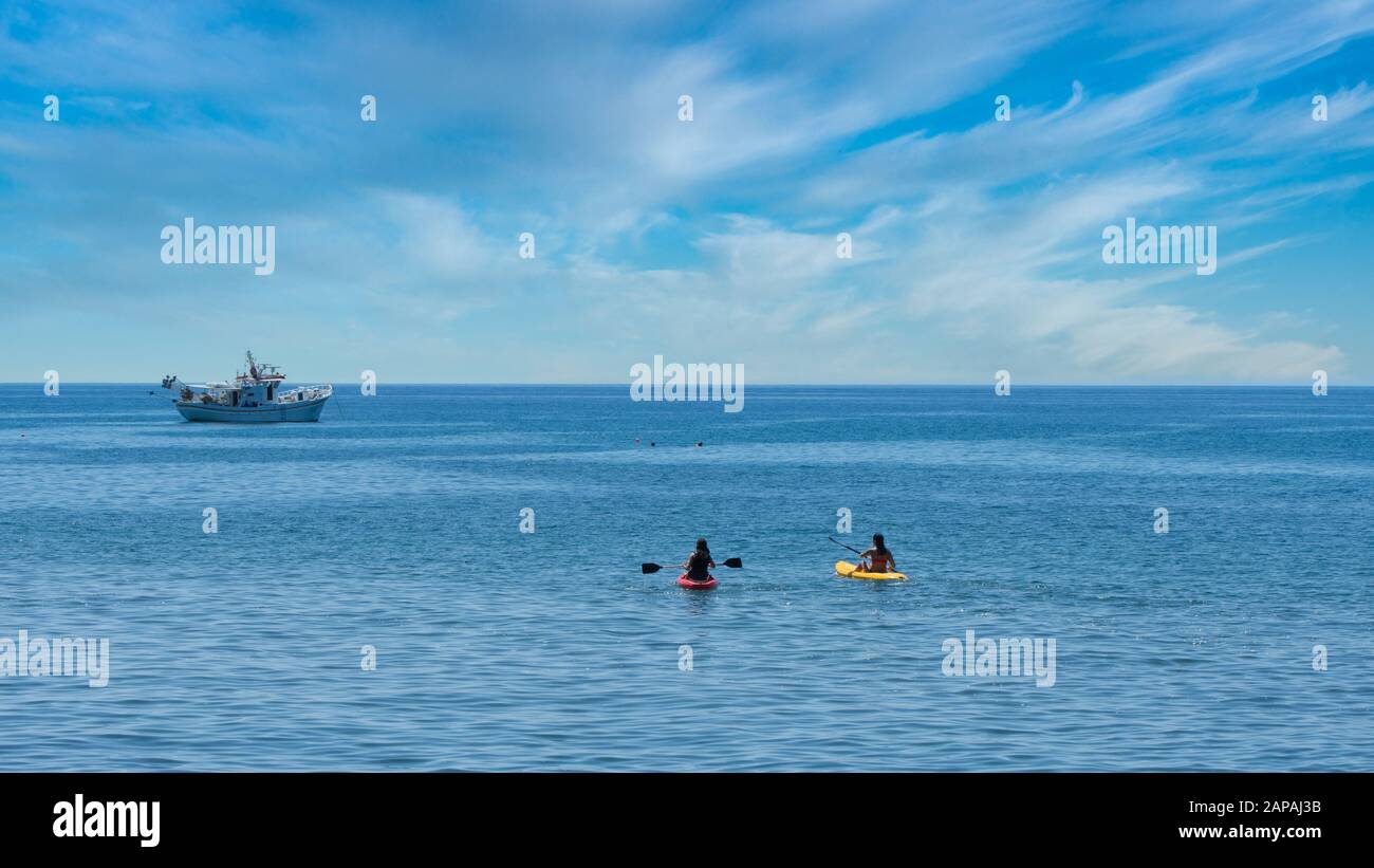 Deux Kayakistes avec bateau de pêche grec à l'ancre en arrière-plan au large de la côte des îles de Lesvos en Grèce Banque D'Images