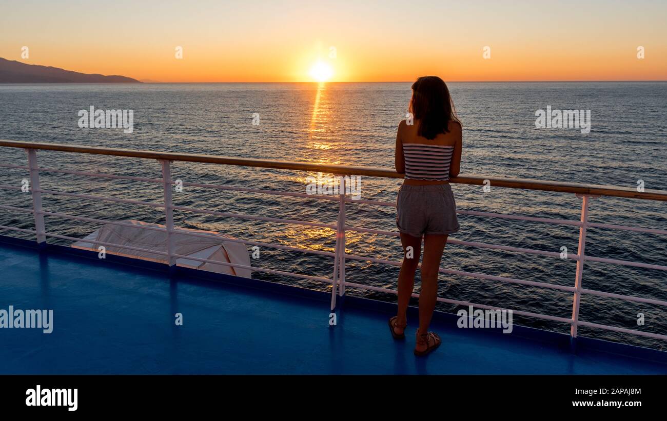 Un adolescent asiatique en métro se tenant sur la terrasse du ferry en regardant le coucher du soleil sur le ferry à destination de Lesvos Banque D'Images