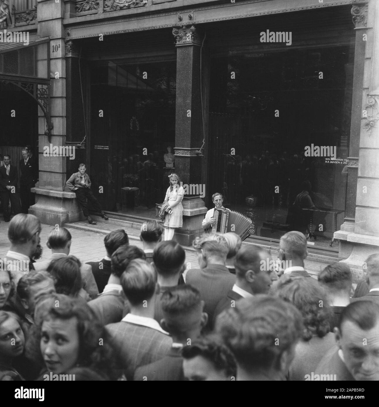 Les divertissements populaires à Amsterdam. Rép. Des diverses festivités liées à la libération dans la capitale Description: [Accordéoniste pour la grande fenêtre de la Royal Furniture Factory et Magaijn H.F. Jansen en Zoon aan de Spui. Une fille pend derrière lui contre un pilier Date: 28 juin 1945 lieu: Amsterdam, Noord-Holland mots clés: Festivals de libération, seconde Guerre mondiale Banque D'Images