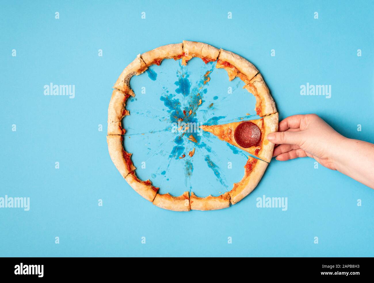 Femme prenant une tranche de pizza salami et de croûte de pizza restes, sur fond bleu. Plat de manger de la pizza pepperoni. Dernière tranche de pizza et de croûte. Banque D'Images