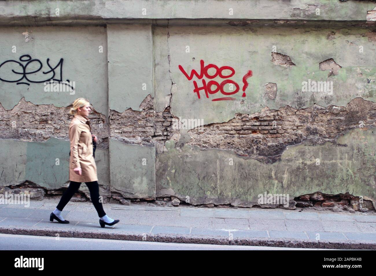 Une jeune femme qui se promenait dans la rue à Vilnius, en Lituanie, alors que la caméra est centrée sur le texte rouge sur le mur vert Banque D'Images