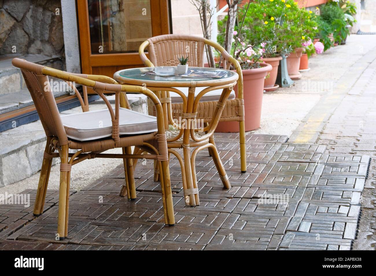 Table en rotin et chaises dans la véranda extérieure d'été de la maison à café. Pots de fleurs avec plantes vertes en arrière-plan. Banque D'Images