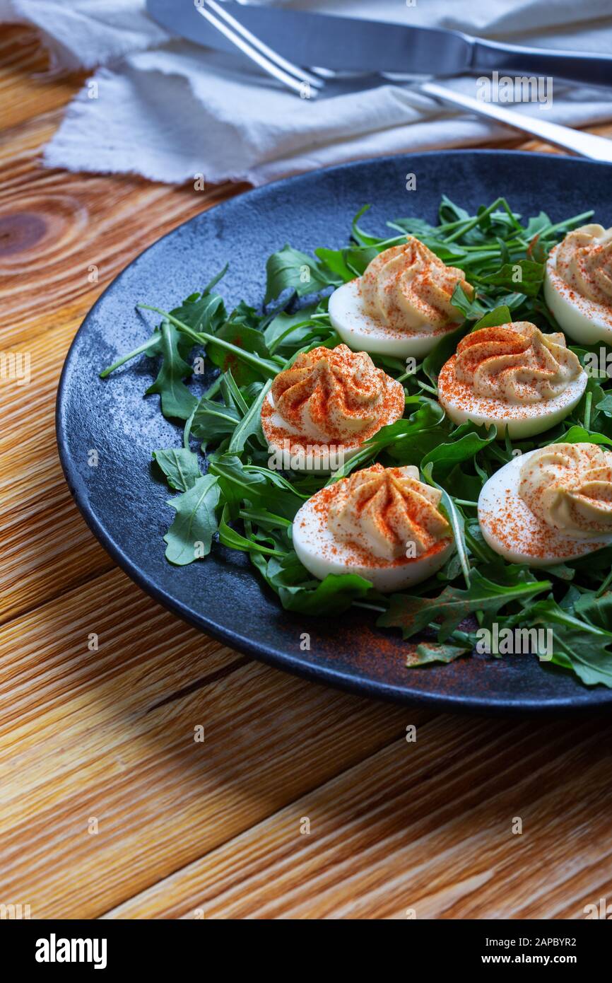 Œufs dévorés au paprika sur salade d'arugula fraîche dans la plaque rurale noire sur table en bois, appétissant végétarien sain ou en-cas près Banque D'Images