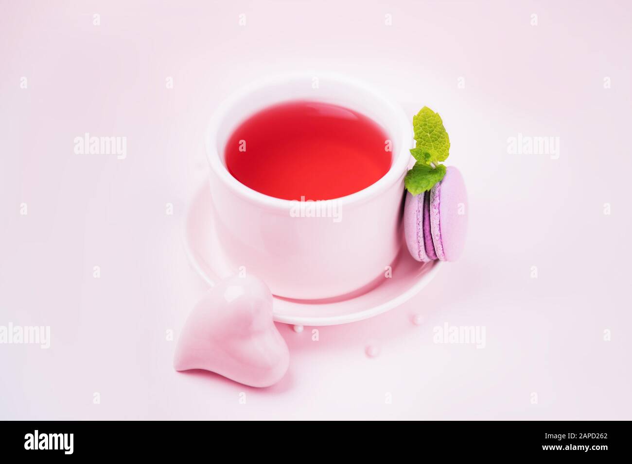 Thé aux fruits, macaron blackberry ou macaron et coeur en céramique rose sur fond rose pâle, espace copie Banque D'Images