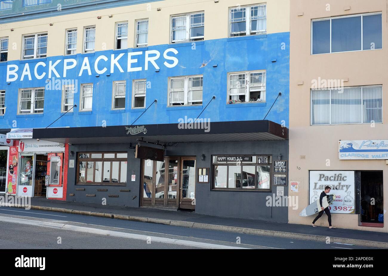 Un surfeur passe devant un hôtel Bondi Backpackers, des vitrines de magasins et des appartements sur Campbell Parade Banque D'Images