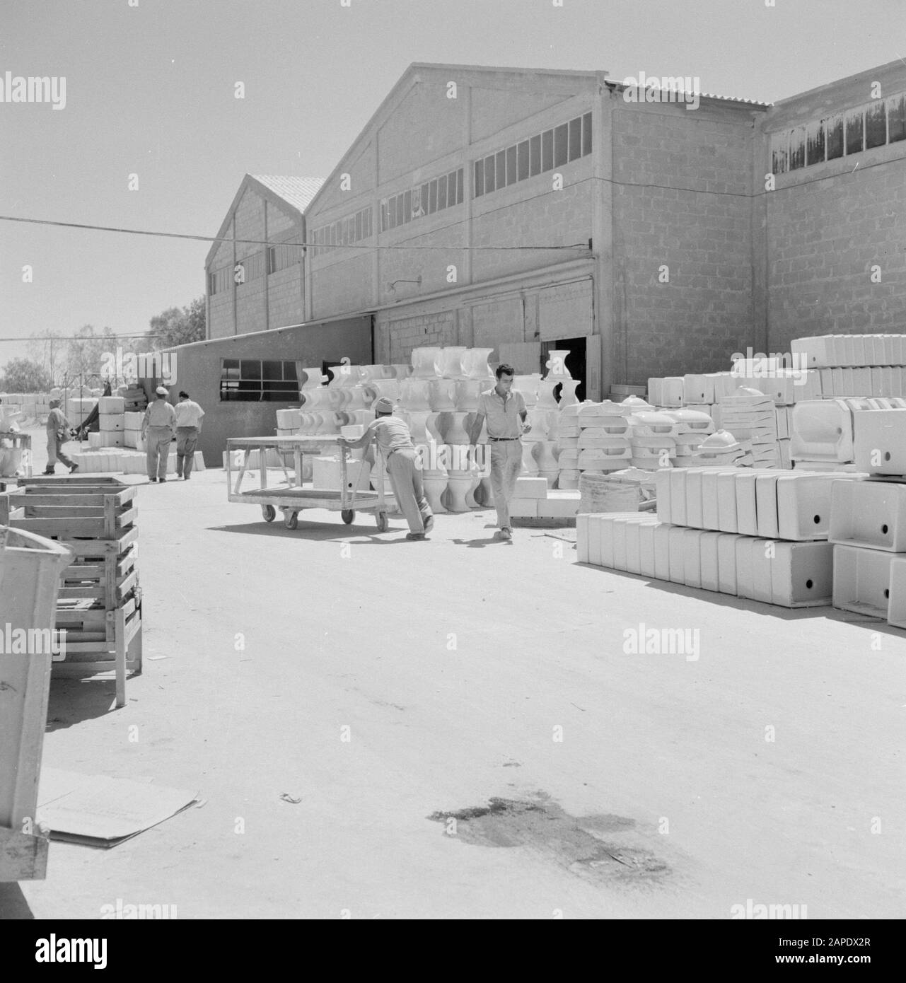 Travailleurs sur le site d'une usine de céramique à Bersjeba dont on pousse une voiturette. Sur le côté se trouvent des lavabos et des pots de toilettes huilés Date: 1 janvier 1964 lieu: Haïfa, Israël mots clés: Travailleurs, usines, industrie, céramique, transport, lavabos Banque D'Images