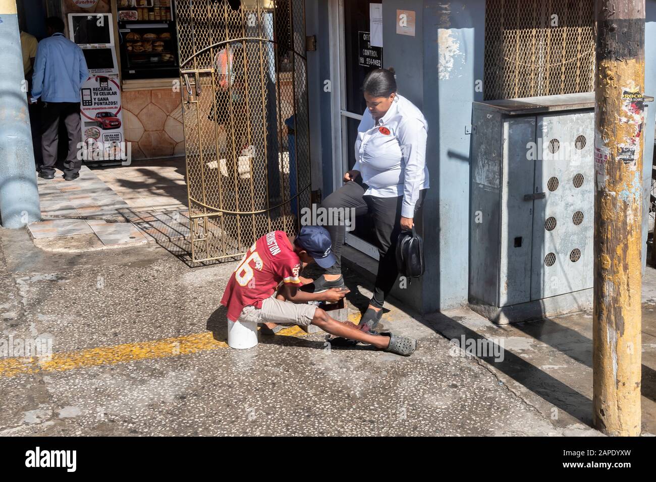 Un garçon, un polisseur de chaussures de rue, est des chaussures de nettoyage pour une travailleuse féminine, République dominicaine Banque D'Images