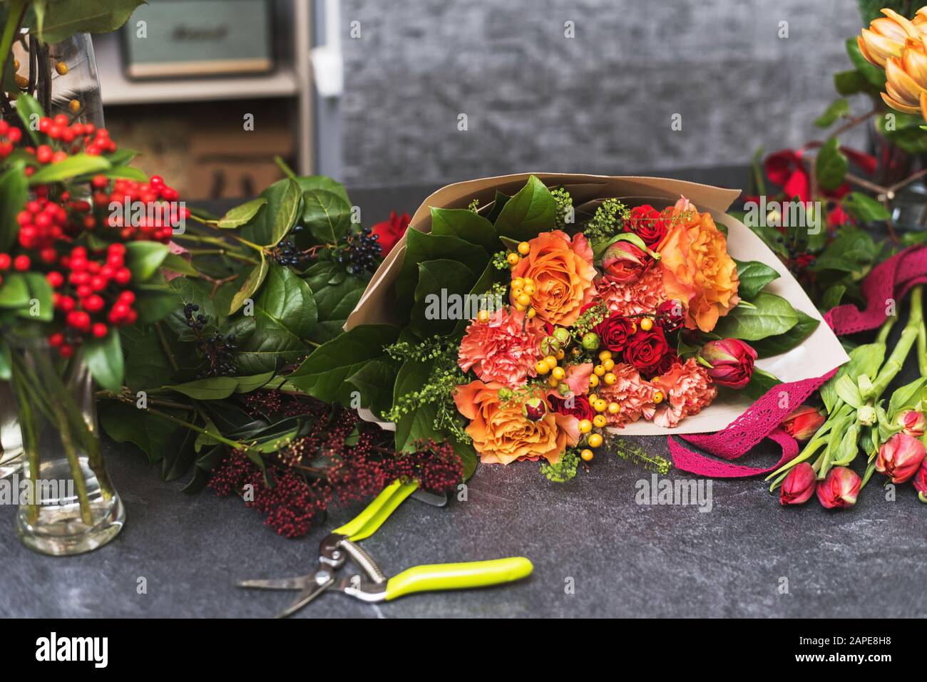 Bouquet de fleurs rouge et orange sur surface en pierre. Un bouquet assemblé de fleurs dans un emballage en papier à côté de ciseaux ou d'un pruner de fleuriste. Banque D'Images