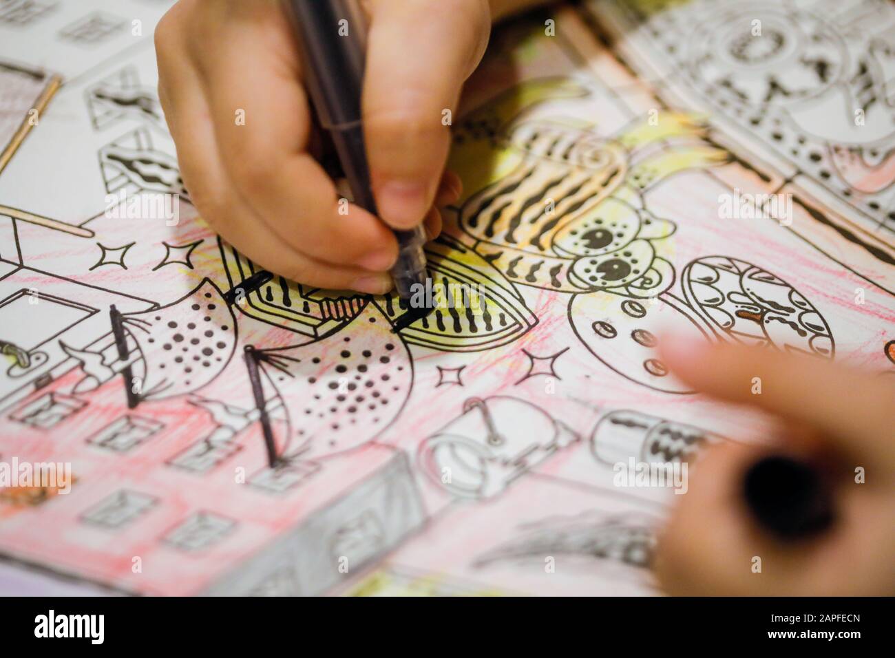 Faible profondeur de champ (mise au point sélective) et image macro avec la main d'une petite fille utilisant un sharpie pour dessiner sur un livre de coloriage. Banque D'Images