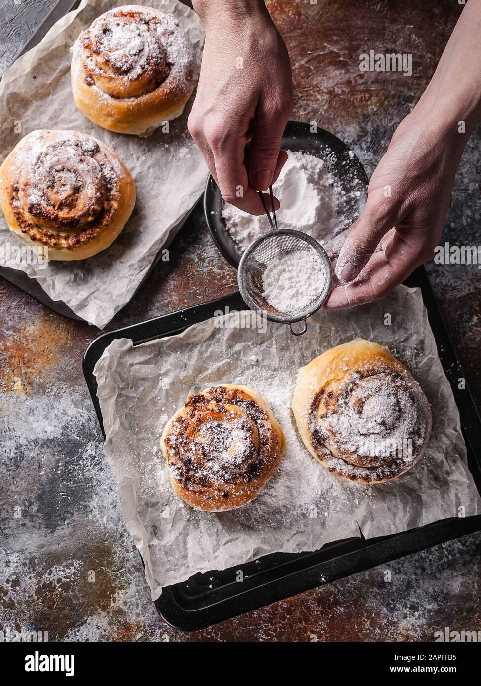 Les mains féminines saupoudrer de sucre en poudre avec des petits pains à la cannelle maison et de la crème au chocolat. Cuisine scandinave. Style Hyugge Banque D'Images