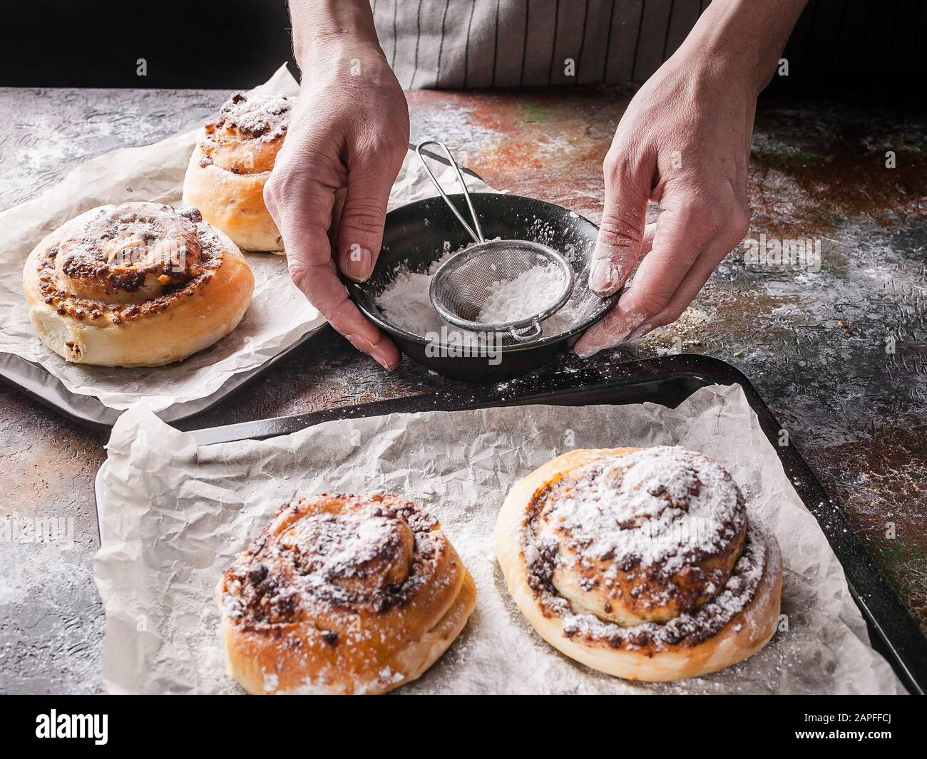 Les mains féminines saupoudrer de sucre en poudre avec des petits pains à la cannelle maison et de la crème au chocolat. Cuisine scandinave. Style Hyugge Banque D'Images