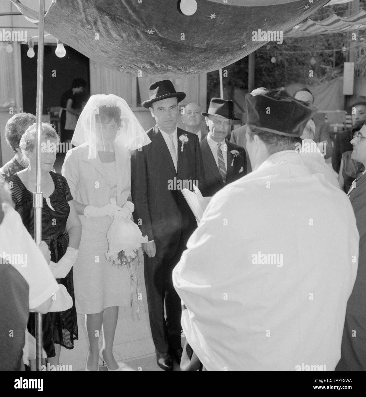 Israël 1964-1965: Tel Aviv, mariage Description: La mariée et le marié se tiennent sous le Choepa alors que le rabbin lit à haute voix Annotation: La mariée et le marié (Kallah et Chatan) sont finalement ensemble sous un Choepa (couvert de mariage) après sept fois que la mariée a encerclé le Choepa et son marié, qui est principalement placé à l'extérieur et que leur "maison ouverte" (hospitalité), date proposée: 1964 lieu: Israël, tel Aviv mots clés: Couvert, bouquet, mariée, marié, sauge, lumières de fête, peignoirs, coiffures, invités de mariage, cérémonies de mariage, religion juive, rabbins, voiles Banque D'Images