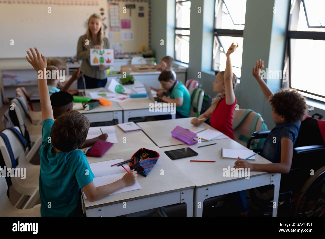 Groupe d'écoliers levant les mains dans une classe de l'école primaire Banque D'Images