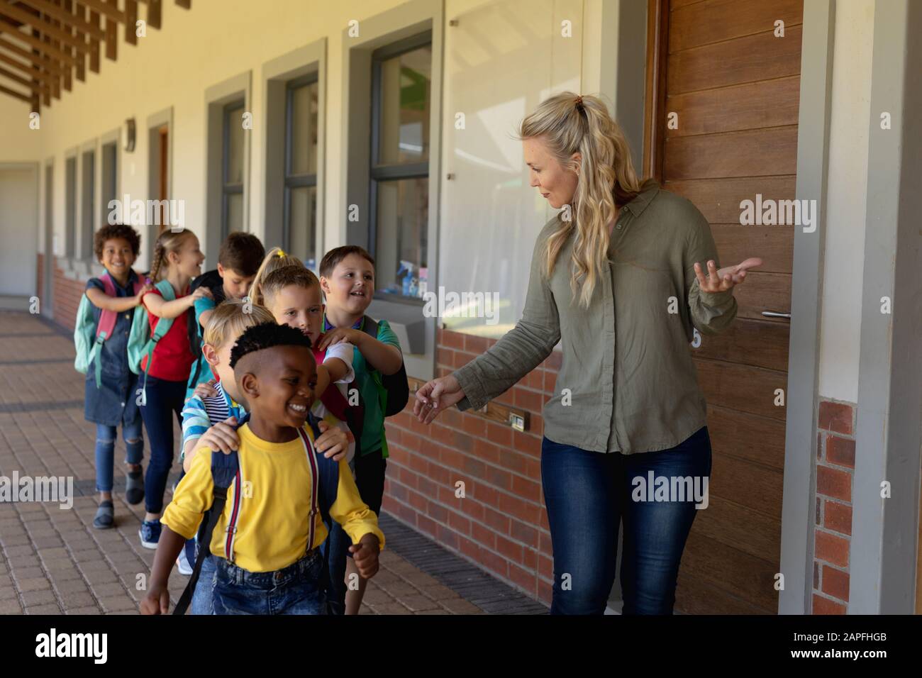 Professeur de femme avec de longs cheveux blonds conduisant un groupe d'écoliers dans une école primaire Banque D'Images